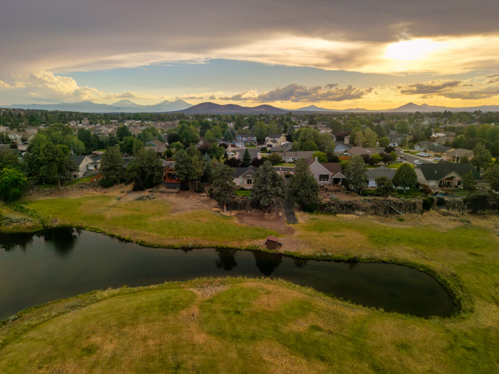 Aerial real estate photo of Central Oregon homes along a pond with the Cascade Mountains at sunset